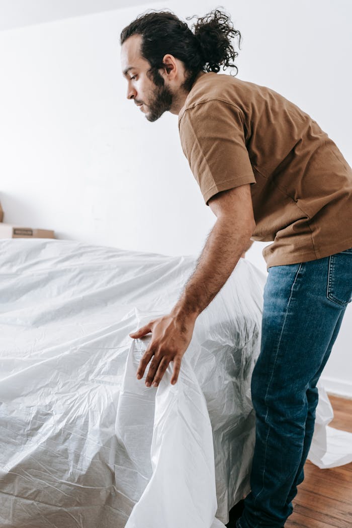 about-02 A man covers a couch with a white protective sheet while preparing to move.
