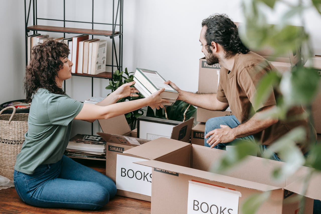 hero-02 A couple organizing and packing books in cardboard boxes indoors, preparing for a move.