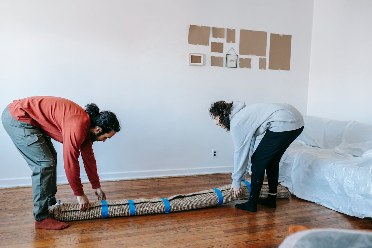 hero-01 Two adults carefully roll up a rug while packing up in a bright, minimal living room.